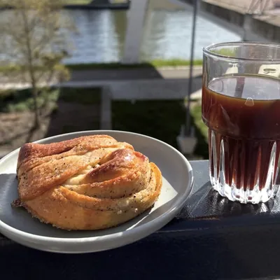 Kaneelbroodje met een glas filterkoffie op de reling, met het kanaal op de achtergrond